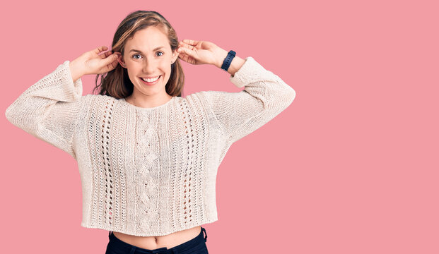 Young beautiful blonde woman wearing casual sweater smiling pulling ears with fingers, funny gesture. audition problem
