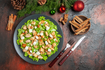 top view caesar salad on oval plate fork knife bowl with dried crust cinnamon sticks on dark red background