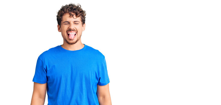Young handsome man with curly hair wearing casual clothes sticking tongue out happy with funny expression. emotion concept.