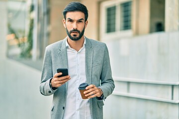 Young hispanic businessman with serious expression using smartphone and drinking coffee at the city.