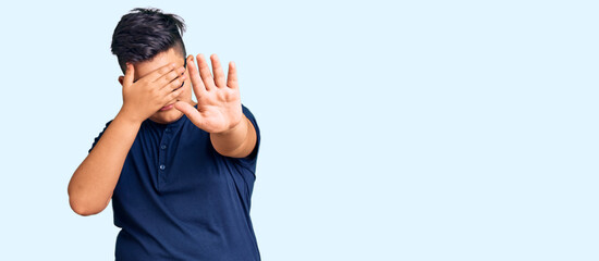 Little boy kid wearing casual clothes and glasses covering eyes with hands and doing stop gesture with sad and fear expression. embarrassed and negative concept.