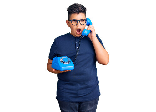 Little boy kid using vintage telephone scared and amazed with open mouth for surprise, disbelief face