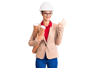 Young beautiful woman wearing architect hardhat and glasses holding blueprints doing ok sign with fingers, smiling friendly gesturing excellent symbol