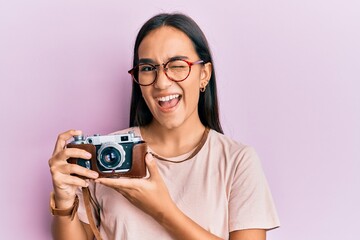 Young asian woman holding vintage camera winking looking at the camera with sexy expression, cheerful and happy face.