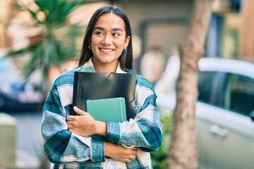Young latin student girl smiling happy holding folder at the city.