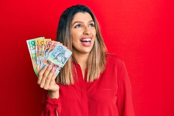Beautiful brunette woman holding australian dollars looking away to side with smile on face, natural expression. laughing confident.