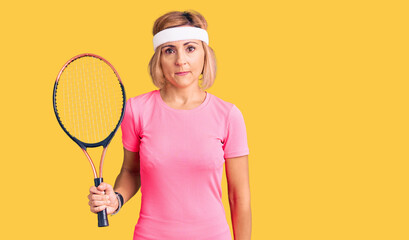 Young blonde woman playing tennis holding racket thinking attitude and sober expression looking self confident
