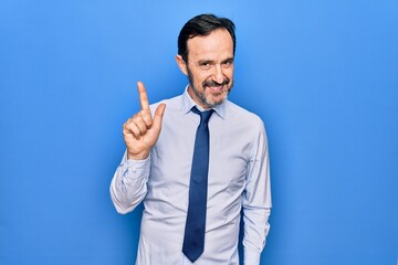 Middle age handsome business man wearing elegant tie standing over isolated blue background smiling with an idea or question pointing finger up with happy face, number one