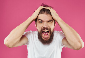 An angry man touches his head with his hands on a pink background Copy Space