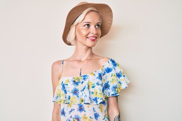 Young blonde woman with tattoo wearing summer hat looking away to side with smile on face, natural expression. laughing confident.