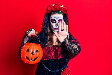 Young woman wearing day of the dead costume holding pumpkin with open hand doing stop sign with serious and confident expression, defense gesture