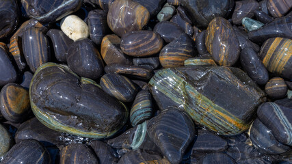 Top view of sea rocks or granite pebbles while getting light waves making white bubbles and light reflection. Background of wet stone at sea shore