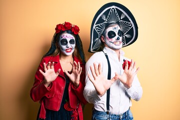 Couple wearing day of the dead costume over yellow disgusted expression, displeased and fearful doing disgust face because aversion reaction. with hands raised