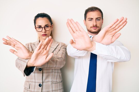 Beautiful couple wearing business clothes rejection expression crossing arms and palms doing negative sign, angry face