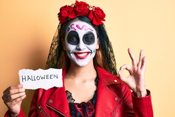 Woman wearing day of the dead costume holding halloween paper doing ok sign with fingers, smiling friendly gesturing excellent symbol
