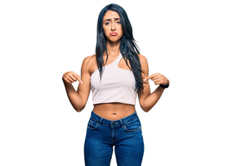 Beautiful hispanic woman wearing casual clothes pointing down looking sad and upset, indicating direction with fingers, unhappy and depressed.