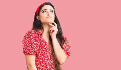 Fototapeta premium Brunette teenager girl wearing summer dress with hand on chin thinking about question, pensive expression. smiling and thoughtful face. doubt concept.