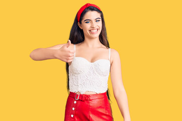 Brunette teenager girl wearing elegant look doing happy thumbs up gesture with hand. approving expression looking at the camera showing success.