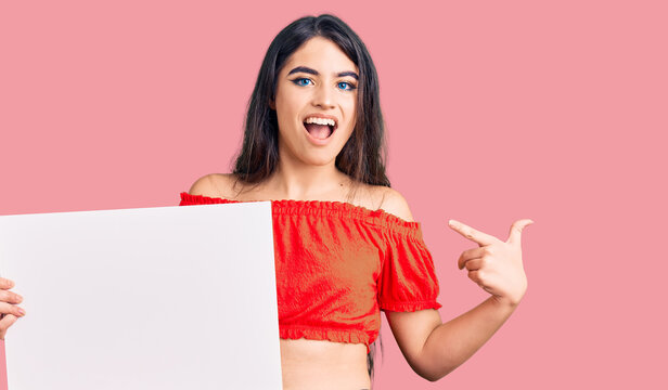 Brunette teenager girl holding blank empty banner smiling happy pointing with hand and finger