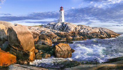Peggy's Cove lighthouse at sunset. Photo taken from the shore below with low sun shining on rocky...