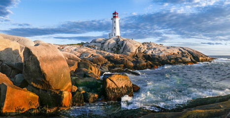 Peggy's Cove lighthouse at sunset. Photo taken from the shore below with low sun shining on rocky...
