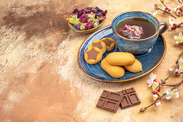 Top view of various biscuits a cup of tea and flowers chocolate bars on mixed color table