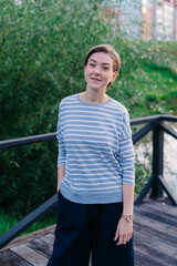 Middle aged woman with a short haircut in a striped shirt posing by the lake in a park