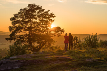 Obraz na płótnie Canvas A young couple admires the summer sunset on top of Paasonwoori Mount. Sortavala, Karelia