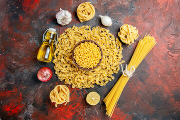 Top view of uncooked pastas in various forms as spaggeti garlic and onion oil bottle on mixed color background