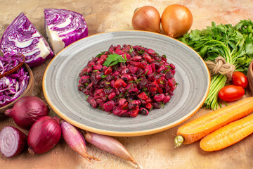 top view a ceramic plate with fresh beet salad and ingredients for its preparation on a wooden table