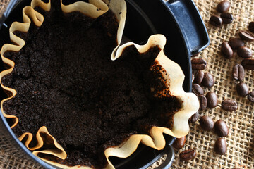 An image of a used coffee filter with coffee basket and coffee beans on burlap.