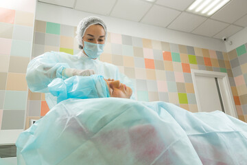 Woman doctor in a blue robe performs surgical cosmetic surgery on the face of a man