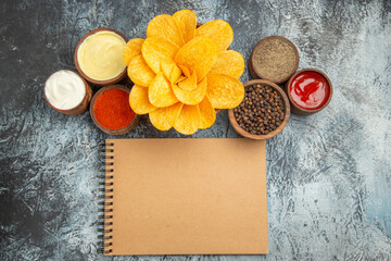 Horizontal view of homemade potato chips decorated like flower shaped and notebook on gray background