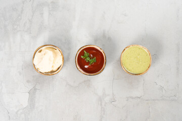 A set of three sauces in small round saucers on a light neutral concrete table. Ketchup, mayonnaise cheese sauce and garlic sauce with herbs.