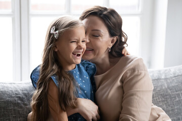 Close up happy mature grandmother and granddaughter hugging, enjoying tender moment, leisure time together, sitting on cozy couch at home, smiling middle aged woman and little girl cuddling