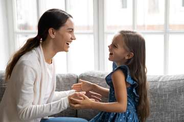 Close up overjoyed mother and little daughter playing patty cake, sitting on couch together, happy young mum and adorable girl child having fun, spending leisure time at home, involved in active game