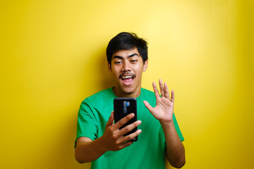 Asian man taking selfie photo or doing a video call at home, smiling to camera and waving