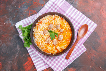 Overhead view of delicious chicken soup with noodles greens and spoon on pink stripped towel on dark background