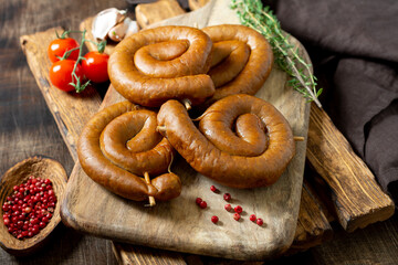 Spiral smoked sausages on a serving Board on a brown wooden table. Spiral sausages. Homemade meat fried sausages	