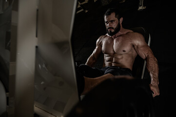 Fototapeta na wymiar strong young bearded caucasian man workout training in leg press machine in dark fitness gym