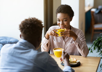 Handsome black man with his girlfriend enjoying aromatic coffee and having friendly conversation at city cafe