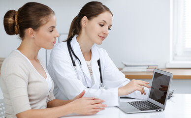 Doctor and patient are sitting and discussing health examination results while using laptop computer. Health care, medicine and good news concepts