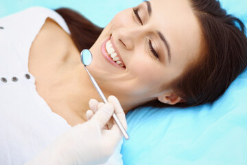 Young female patient visiting dentist office.Beautiful woman with healthy straight white teeth sitting at dental chair with open mouth during oral checkup while doctor working at teeth