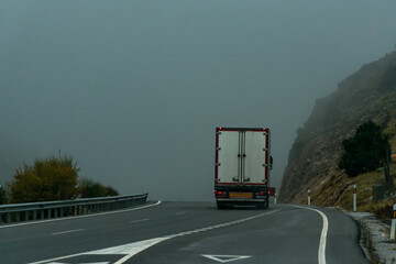 Truck with refrigerated semi-trailer driving on a highway on a foggy day.