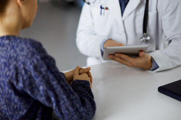 Unknown red-bearded doctor and patient woman discussing current health examination while sitting...