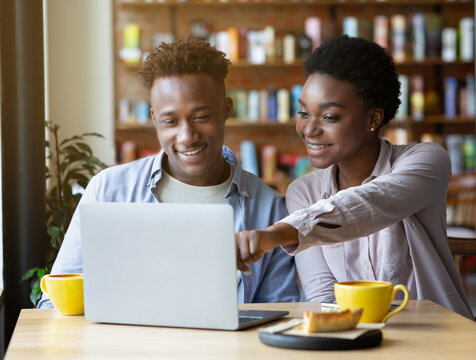 Beauiful black woman pointing at laptop screen, showing something to her boyfriend in coffee shop