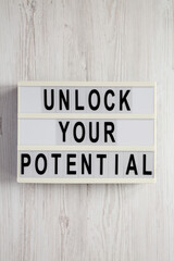 'Unlock your potential' on a lightbox on a white wooden background, top view. Flat lay, overhead, from above.