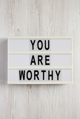 'You are worthy' on a lightbox on a white wooden surface, top view. Flat lay, overhead, from above.