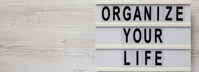 'Organize your life' on a lightbox on a white wooden surface, top view. Flat lay, overhead, from above. Copy space.