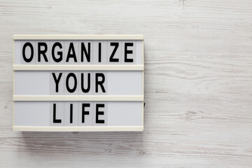'Organize your life' on a lightbox on a white wooden surface, top view. Flat lay, overhead, from above. Copy space.